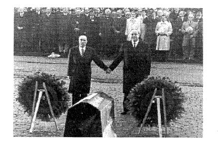 Schwarz-Weiss-Foto: zwei Staatsmaenner geben sich zwischen zwei Kraenzen bei einer Gedenkfeier die Hand
